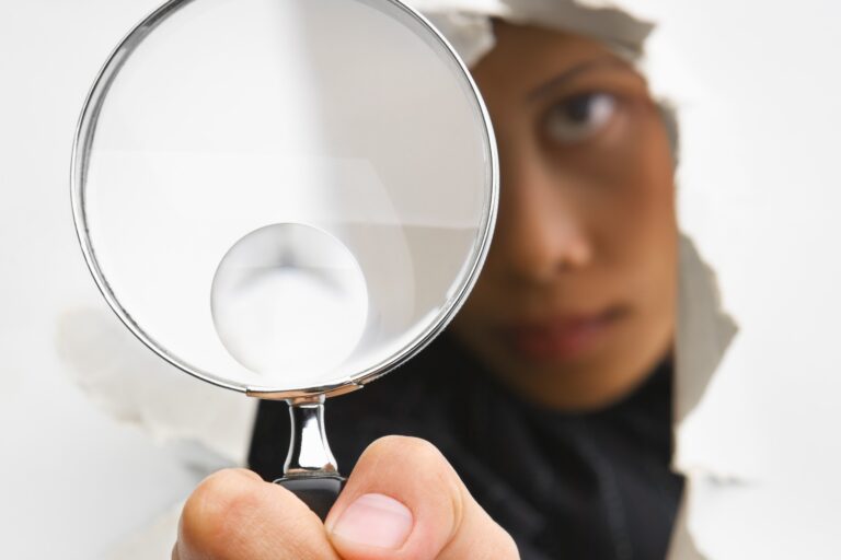 an image of someone holding a magnifying glass with the person on one side of a wall and their hand and the magnifying glass coming through to the other side in the foreground