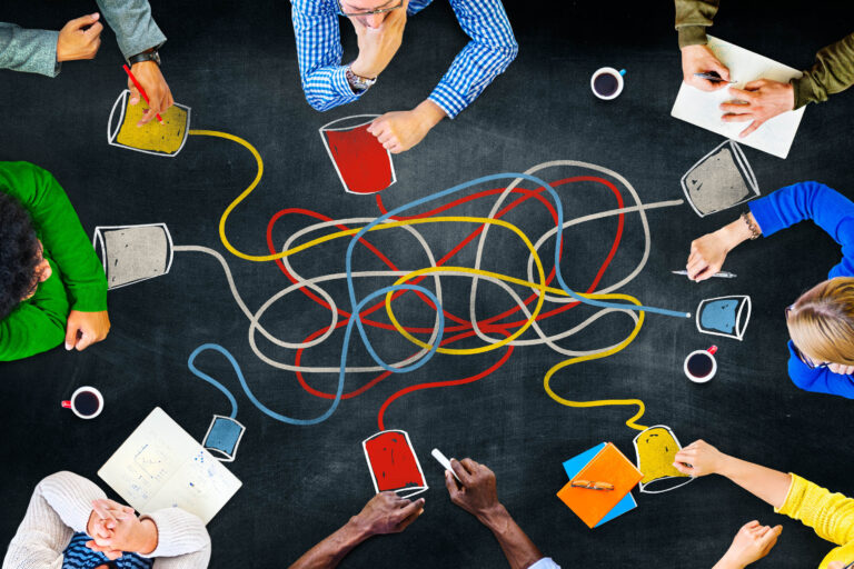 a top-down photo of people sitting at a table having a discussion with a tangle of lines connecting different people