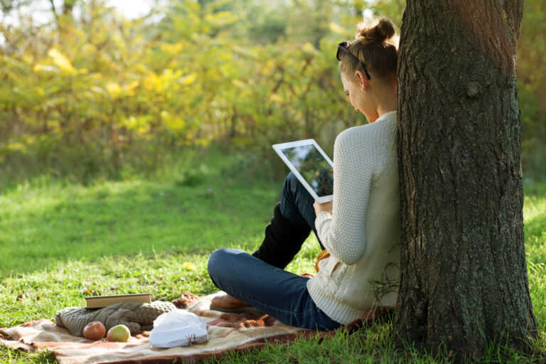 woman sitting against a tree using a tablet