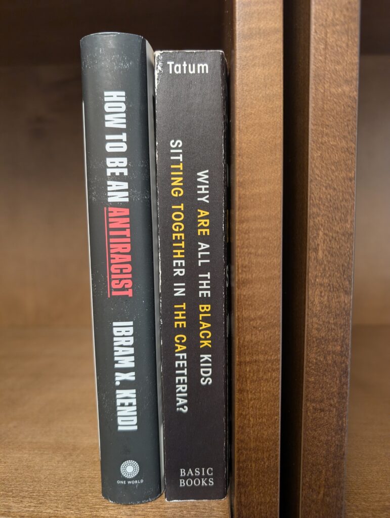 two racial justice oriented books on a bookshelf