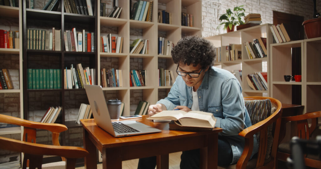 Student doing research in library using a laptop and books